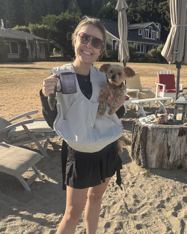 A team member on a beach holding a mug and a small dog
